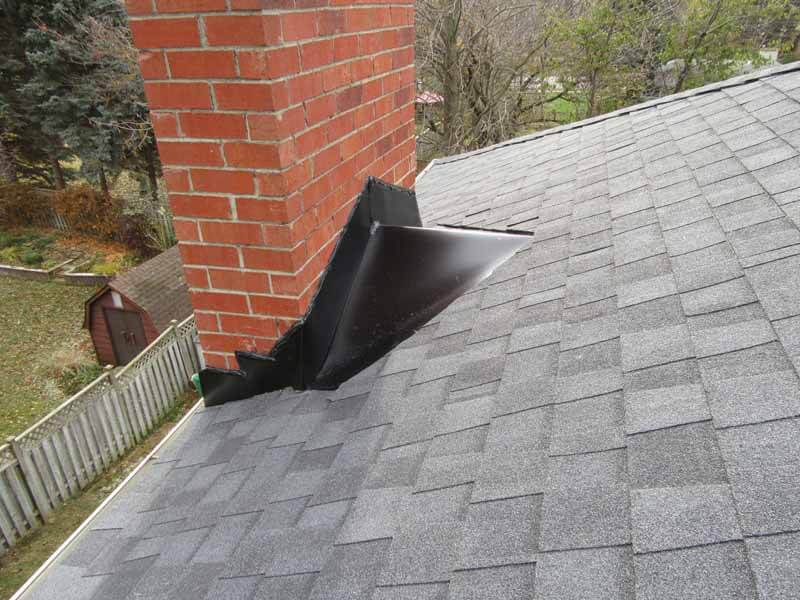 Roof chimney with detached metal flashing on grey asphalt shingles